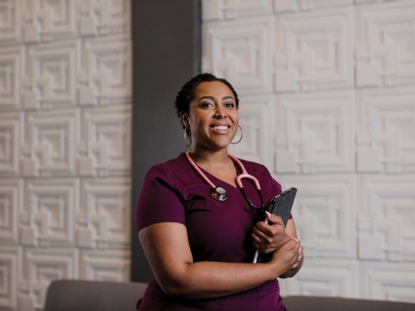 Person in maroon scrubs with a stethoscope, standing in front of a textured wall.
