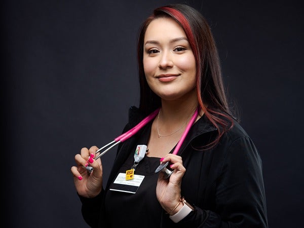 A woman holding a stethoscope, with a badge clipped to her clothing.