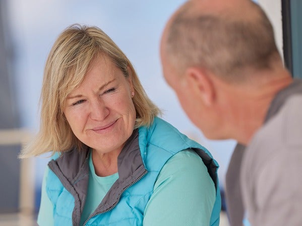 Two people having a conversation outdoors. A woman in a blue vest smiles at a man.
