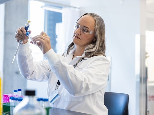 Person in a lab coat using a pipette in a laboratory.