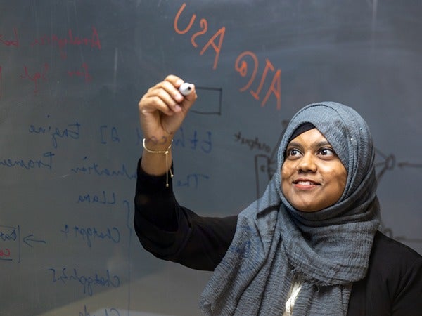 A person writing on a transparent board with colored markers.