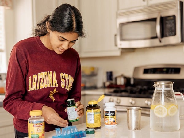 Person in a kitchen organizing vitamins on a counter.