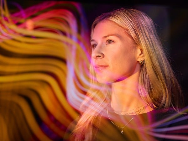 A person with blonde hair surrounded by colorful, abstract light trails.