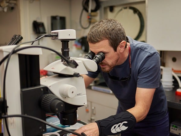 Man looking through a microscope in a laboratory.