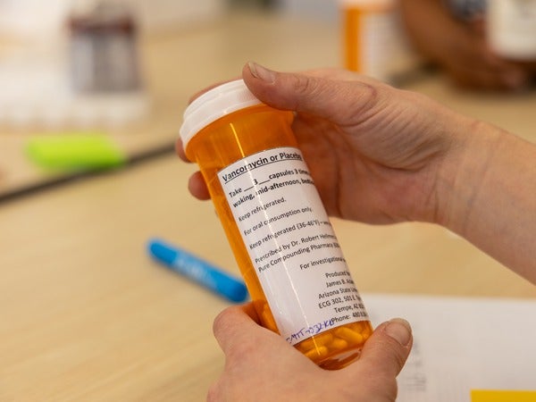 Hands holding an orange prescription pill bottle with visible label text.
