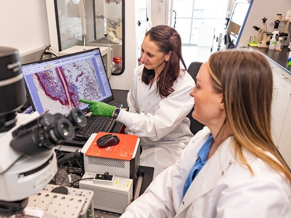 Two people in lab coats examining an image on a computer in a laboratory.