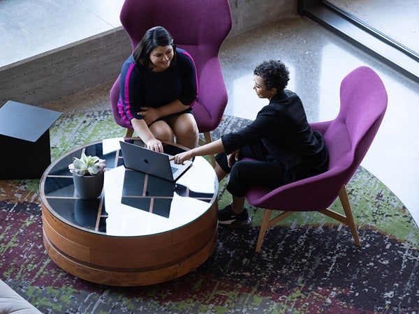 Two people seated in purple chairs around a circular table with a laptop.