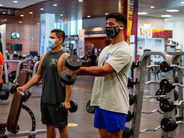 Two people lifting dumbbells in a gym.