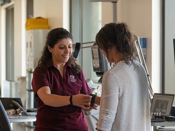 Two women in a lab, one attaching a medical device to the other's wrist.