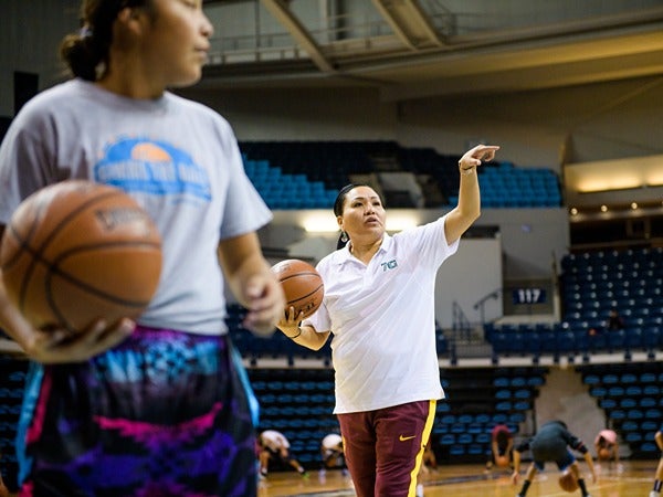Two people in a basketball gym, one giving instructions to the other.