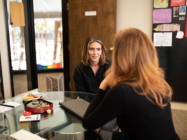 Two women talking at a glass table in an office setting.