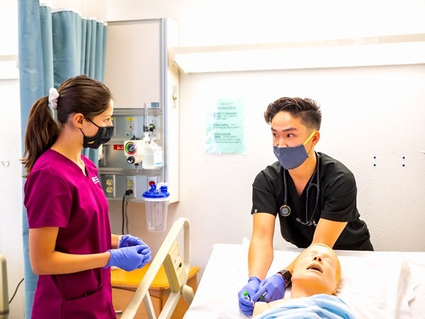 Two people in medical scrubs practicing on a hospital mannequin in a simulation room.