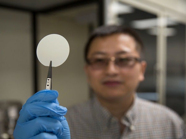 A person holds a white circular object with tweezers in a lab setting.