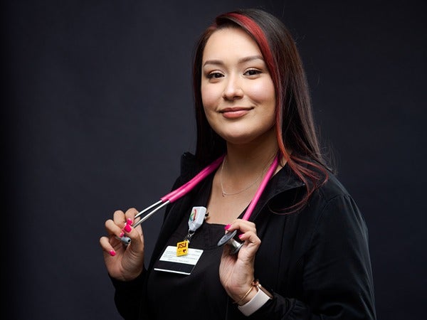 Person holding a pink stethoscope against a dark background.