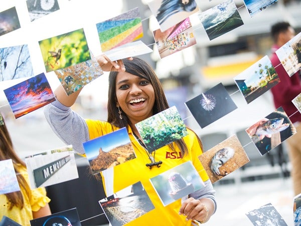 Person in a gold ASU shirt surrounded by hanging photographs.