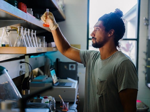 A man in a lab holding a flask with orange liquid.