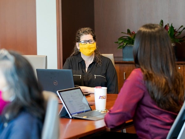 People in a meeting room with laptops and an ASU coffee cup on a conference table.