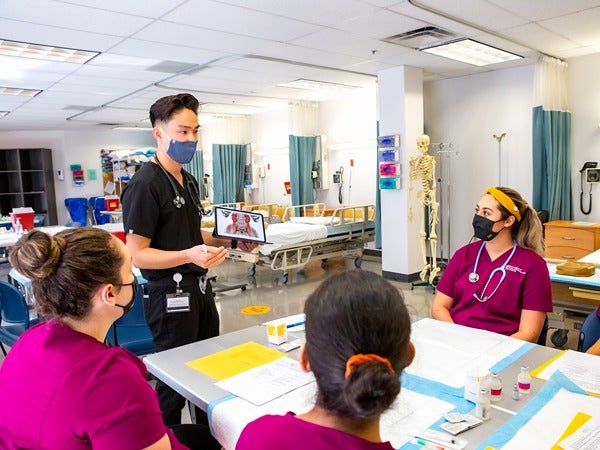 A medical training session with one person presenting to three others seated at a table.