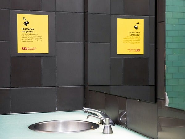 Restroom with dark tiles, a sink, and a yellow poster that says "Pass terms, not germs."