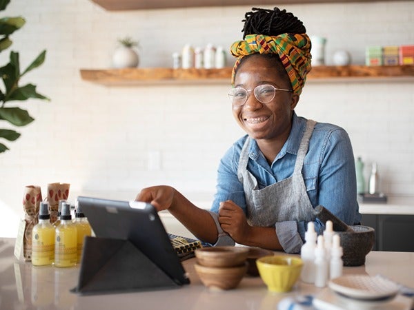 Person wearing a headscarf and apron using a tablet at a counter with various bottles and bowls.