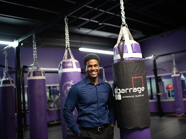 A man in a blue shirt stands next to purple punching bags in a gym.
