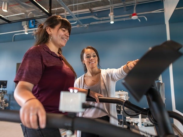 Two women interacting with exercise equipment in a modern fitness facility.