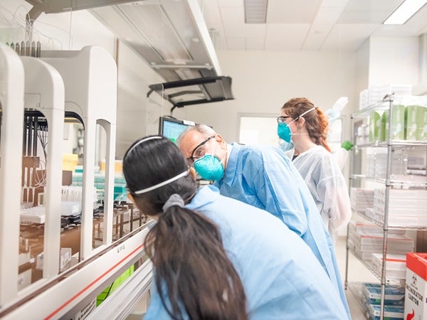 Three people in a lab examining equipment while wearing lab coats and face masks.