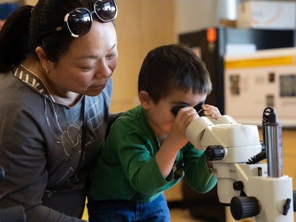 Child looking through a microscope with an adult observing nearby.