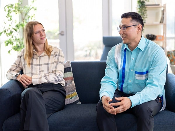 Two people sitting on a blue couch in a well-lit room.