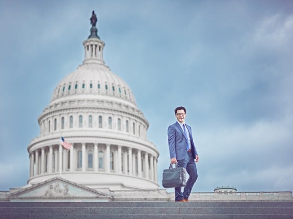 Man in a blue suit with a briefcase walking in front of the U.S. Capitol building.
