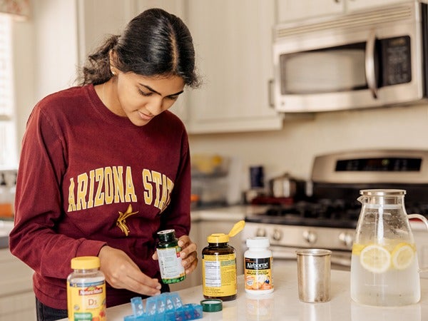 Woman in an Arizona State sweatshirt organizing pills at a kitchen countertop.