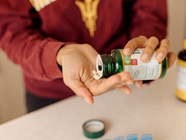 Person pouring pills from a green bottle into their palm.