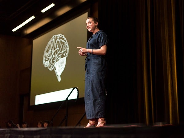 A person on stage in front of a screen showing a brain illustration.