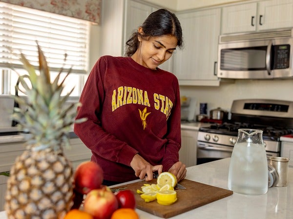 Person slicing a lemon on a cutting board in a kitchen, wearing an "Arizona State" sweatshirt.