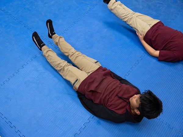 Two people lying on a blue mat performing an exercise.