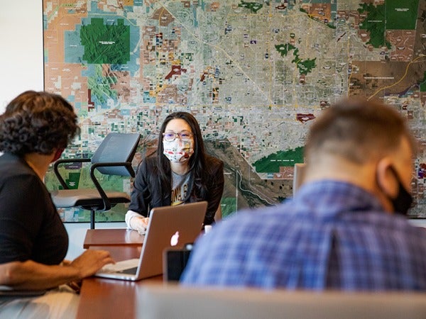 Three people seated around a table with a large map on the wall in the background.