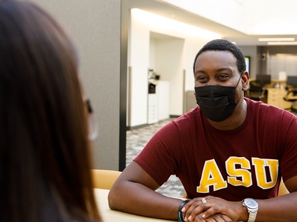 Two people sitting across a table; one wearing an ASU shirt.