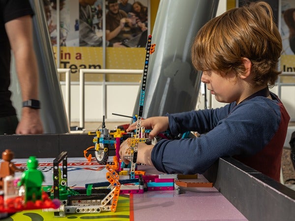 A young child building a colorful LEGO structure at a table.