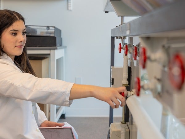 Woman in a lab coat adjusting valves on laboratory equipment.