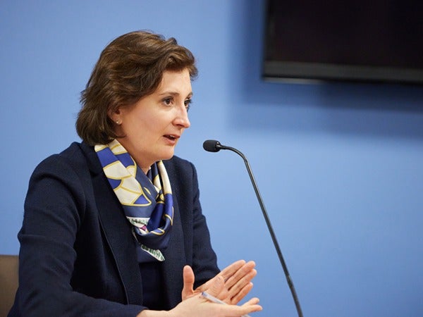 Person in a blue blazer and scarf speaking into a microphone.