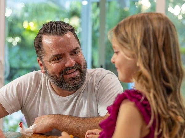 A man and young girl smiling at each other across a table indoors.