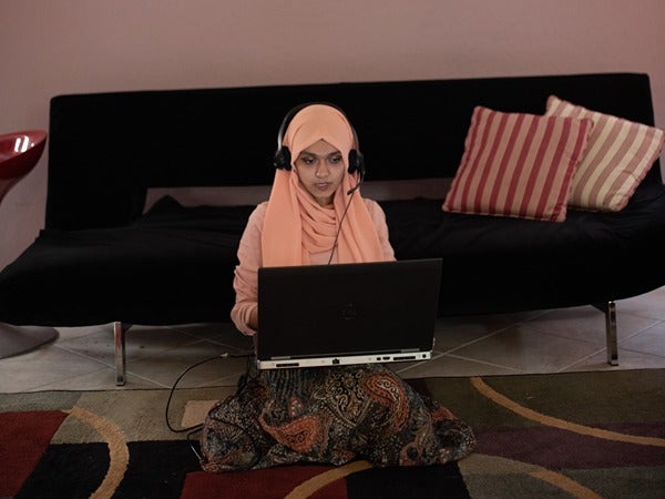 A person with a hijab using a laptop with headphones.