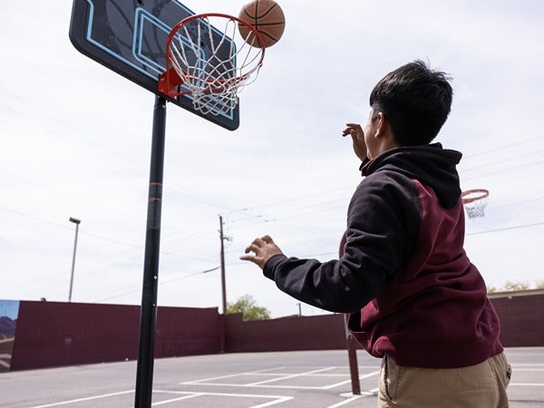A child playing basketball on an outdoor court, shooting towards a hoop.