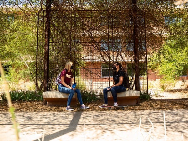 Two people talking on benches in a shaded outdoor area.