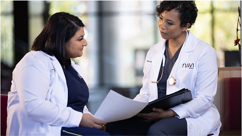 Two healthcare professionals in white coats discussing documents in a medical setting.